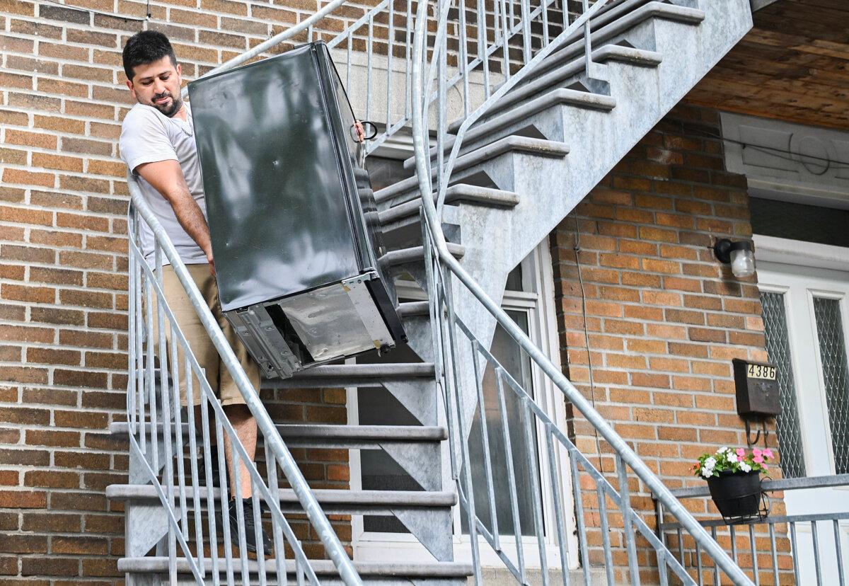 A man carries a mini fridge down a staircase on Quebec's unofficial moving day in Montreal on July 1, 2025. (The Canadian Press/Graham Hughes)