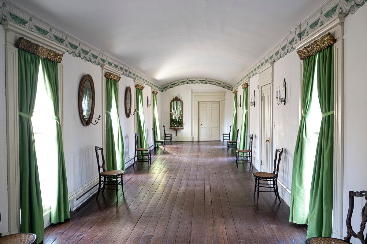 Sherwood Forest’s lengthy 68-foot ballroom features pine floors, on which dances were held. A repeating wallpaper border, representing a valance attached to ornate crown molding, trims the room. Coordinating with the trim are vivid green silk drapes, similar to ones original to the room, that hang from gilt-metal cornices. Some of the antique mirrors are equipped with a candle holder; light from a candle would reflect in the mirror to better illuminate the room. (Sherwood Forest Plantation Foundation)