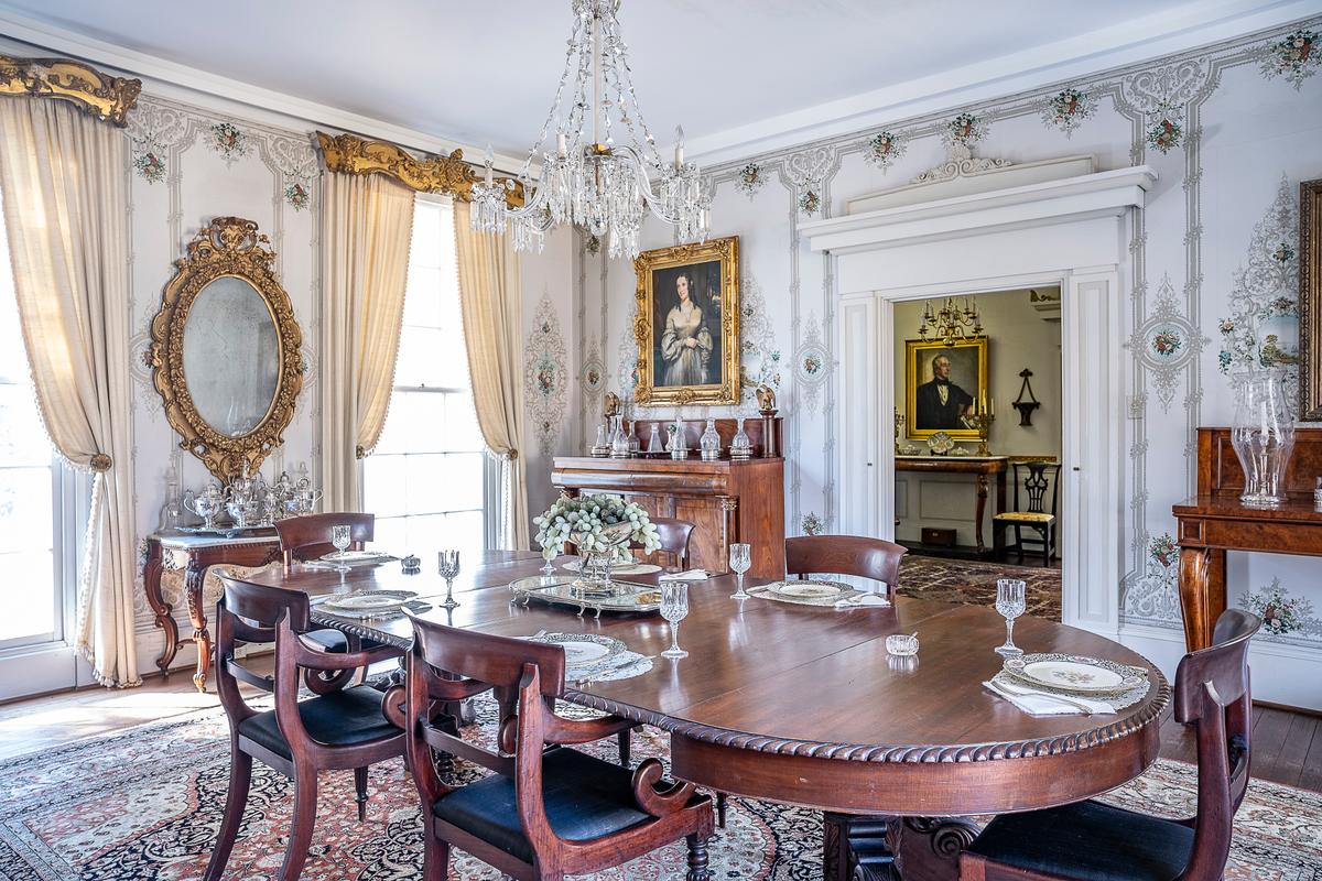 According to Sherwood Forest docent Tim Coin during a December 2025 tour, “The dining room most closely represents the original house when President Tyler lived here.” A rococo revival-style, floral wallpaper is the backdrop for this extravagant room. Coordinating with the intricately carved gilt-wood and gesso (a type of paint coating) cornices over the windows is the equally ornate rococo revival-style mirror and the frame surrounding Julia Gardiner Tyler’s portrait. The mirror is above a rosewood silver-service table original to the house. The mostly mahogany wood furnishings are primarily rococo revival, empire, and American classical style. Many of the antique furnishings are from the ancestral, South Carolina home of Frances Payne Bouknight Tyler. (Sherwood Forest Plantation Foundation)