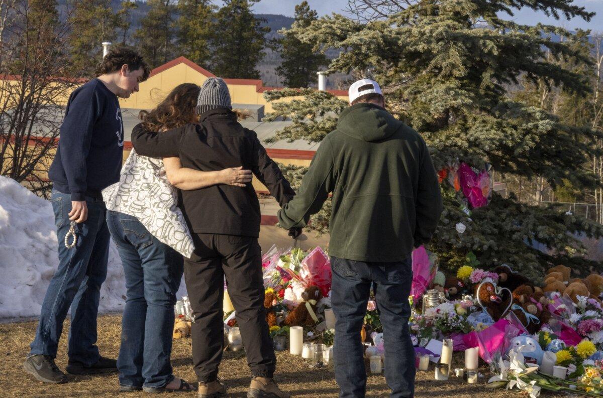 Residents hug as they place flowers at a memorial for the victims of a mass shooting in Tumbler Ridge, B.C., on Feb. 12, 2026. (The Canadian Press/Christinne Muschi)