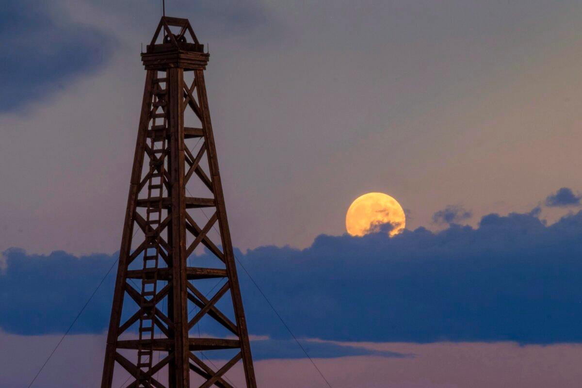 The full moon peeks above the clouds next to a reconstructed 1880s style oil derrick in Casper, Wyo., on July 26, 2018. (J. David Ake/AP Photo)
