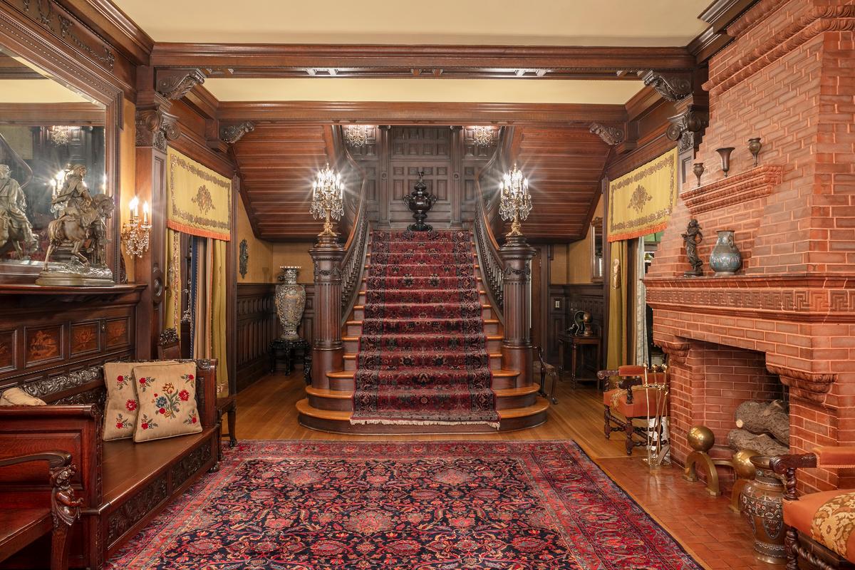 The entryway central hall’s focal point is the wide oak staircase with ornately carved newel posts with attached candelabras. Distinctively, a red brick fireplace is part of the hall. In the 1800s and early 1900s, a wide entry hall could serve as a “room” if necessary, and the fireplace provided heat to anyone congregating in the hall. The hall’s wood paneling, corbels, and ceiling trim are all carved of oak. (McFaddin-Ward House)