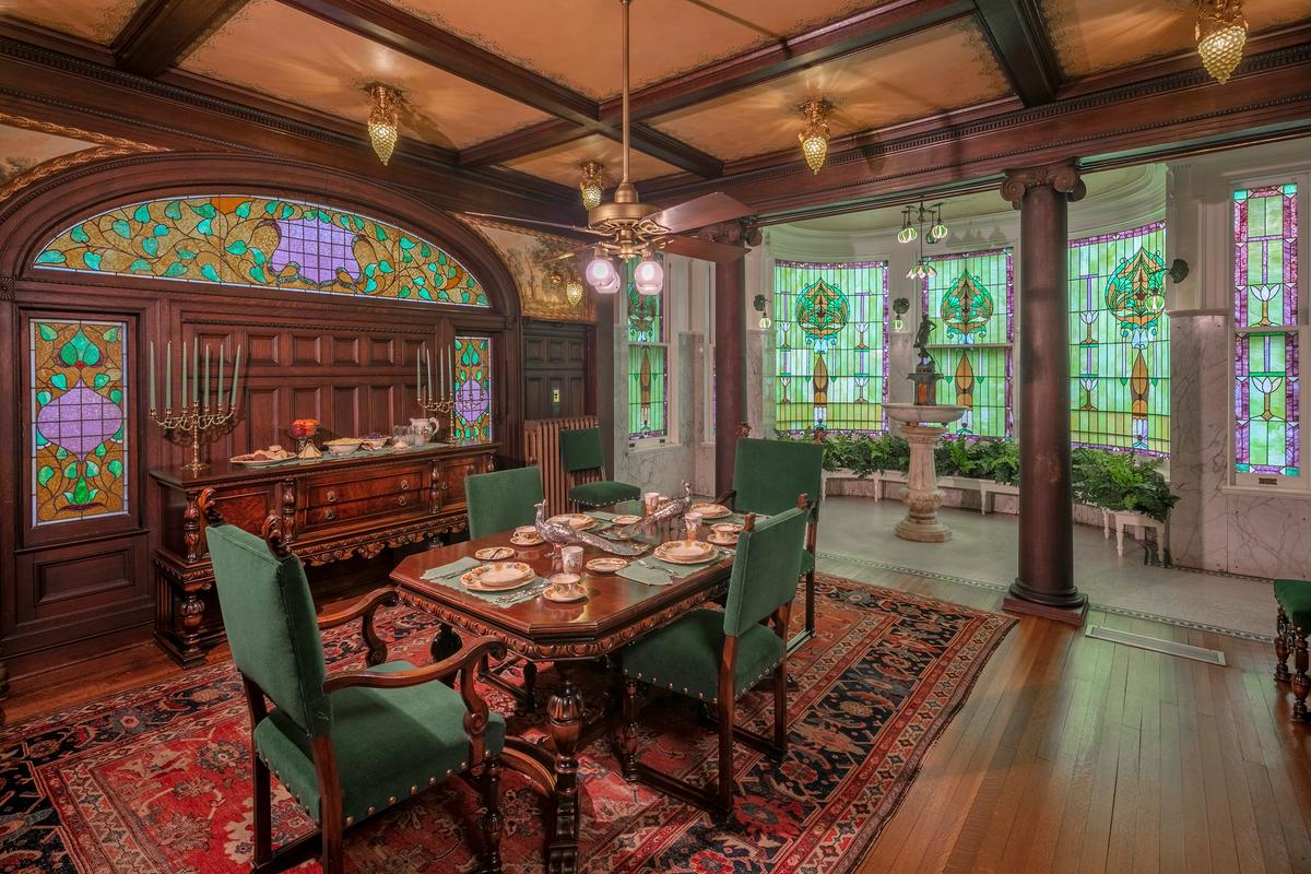 A more casual dining space, deemed the breakfast room, was an addition to the house in 1907. Dominant in this room and the adjoining conservatory are colorful, floral-motif glass in the Art Nouveau style that emerged in the late 1800s. In the middle of the conservatory space is a marble fountain of a bronze maiden pouring water from a pitcher. The sound of water envelopes these rooms. The unique metal and glass lighting fixtures in the shape of grape clumps are in the breakfast area, while a pond lily-shaped fixture is over the fountain in the conservatory. The paneled ceiling, columns, and floors are all oak, while the walls surrounding the art glass in the conservatory are white marble. (McFaddin-Ward House)