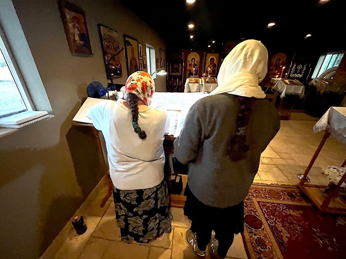 Two women in traditional Russian clothing study from a manuscript before services at Holy Archangels Orthodox Church in Phoenix on Jan. 30, 2026. (Allan Stein/The Epoch Times)