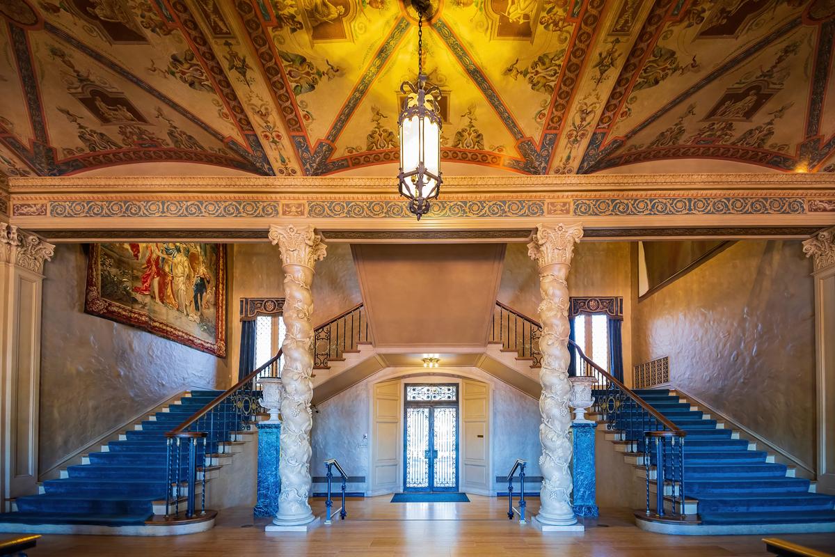 Spiral Solomonic columns adorned with a carved ivy motif and topped with ornamental Corinthian capitals are found in several interior spaces, including at the double staircase, which accesses the grand receiving hall. Floral carvings embellish the beam supported by the columns, and a focal point is the large French-style lantern light fixture hanging from the intricately painted ceiling. A massive tapestry hangs on one of the textured walls. (Kit Leong/Shutterstock)