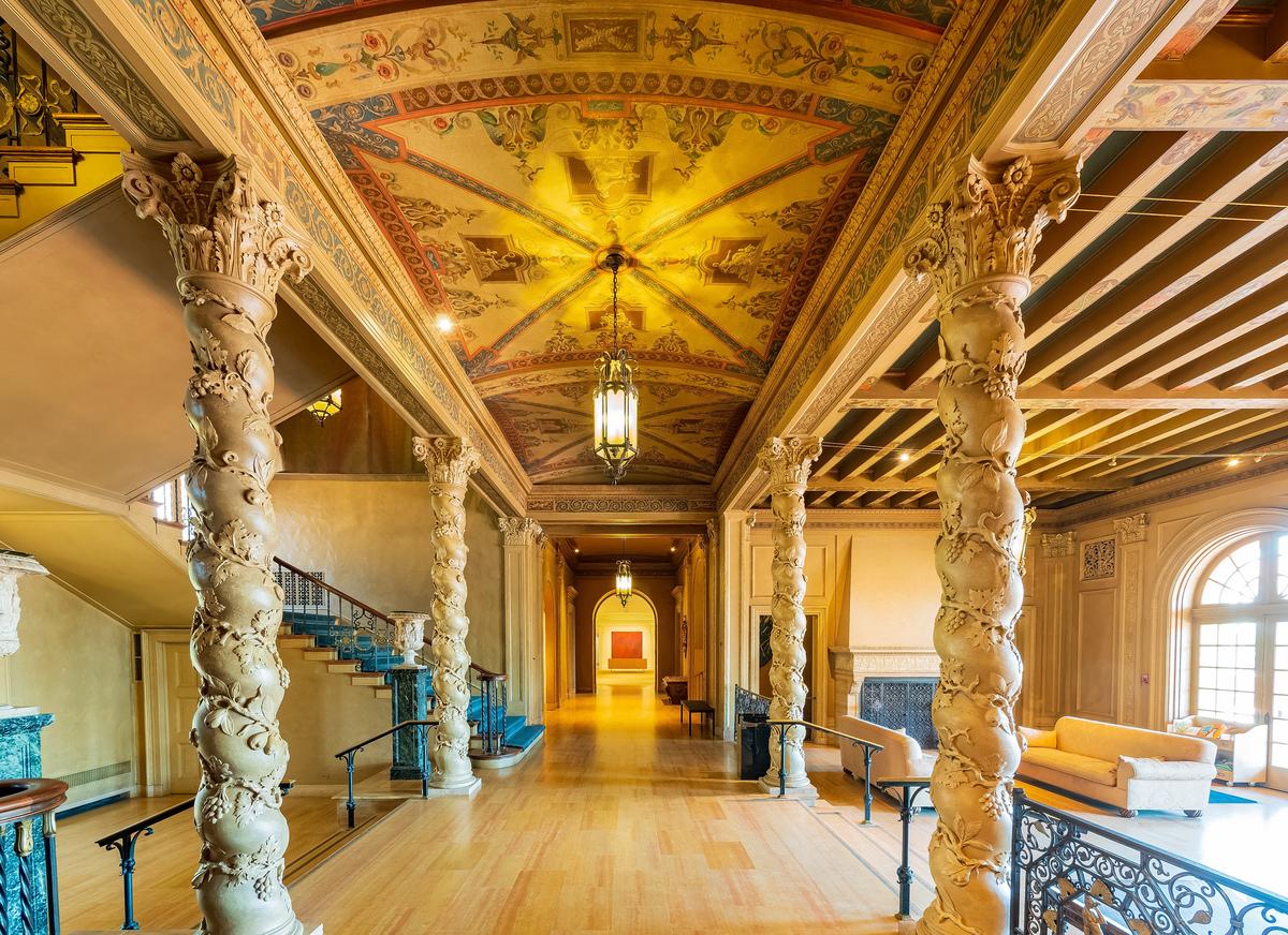 Teak flooring coordinates with the grand receiving hall’s neutral color scheme. Set apart is the frescoed, barrel-vaulted ceiling, which serves as a raised cross-corridor connector between the staircase and a sunlit sitting area. In it, floor-to-ceiling arched windows contrast with a ceiling of painted beams. The Solomonic columns with Corinthian capitals and the mansion’s signature climbing ivy design draw the eye to the room’s artistic ceiling. (Kit Leong/Shutterstock)