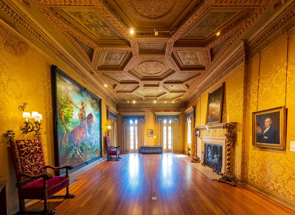 The opulent living room’s most prominent feature is its heavily carved coffered ceiling. Geometric shapes bordered in a carved design are filled with carvings or frescoes. A ship design is showcased in the metal fireplace screen, while the fireplace mantel has a carved classical swag design. The floors are teakwood. (Kit Leong/Shutterstock)