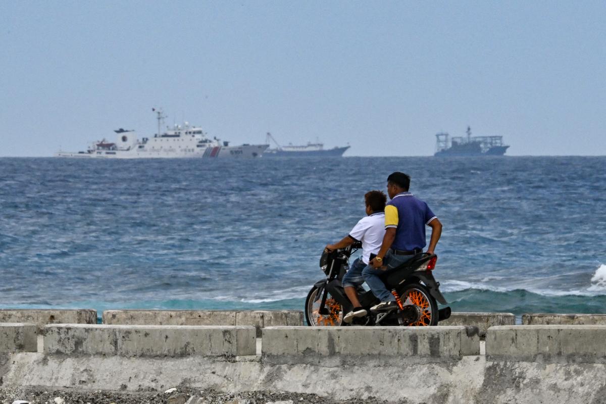 A China Coast Guard ship is seen as residents ride a motorcycle on Thitu Island in the South China Sea on Feb. 21, 2026. (Jam Sta Rosa/AFP via Getty Images)