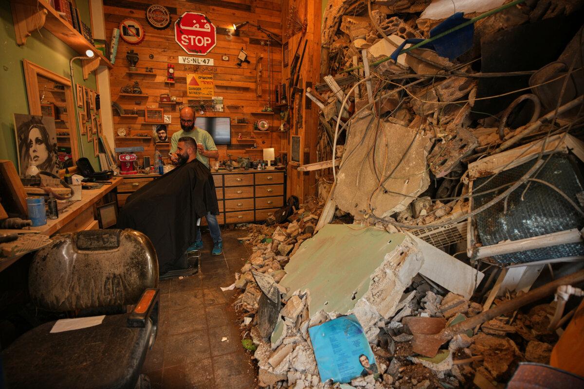 Barber Mohammad Mehdi cuts the hair of customer Ayman Al Zein in his shop, which was damaged in an Israeli airstrike, in Dahiyeh, a suburb of Beirut, Lebanon, on April 18, 2026. (Hassan Ammar/AP)