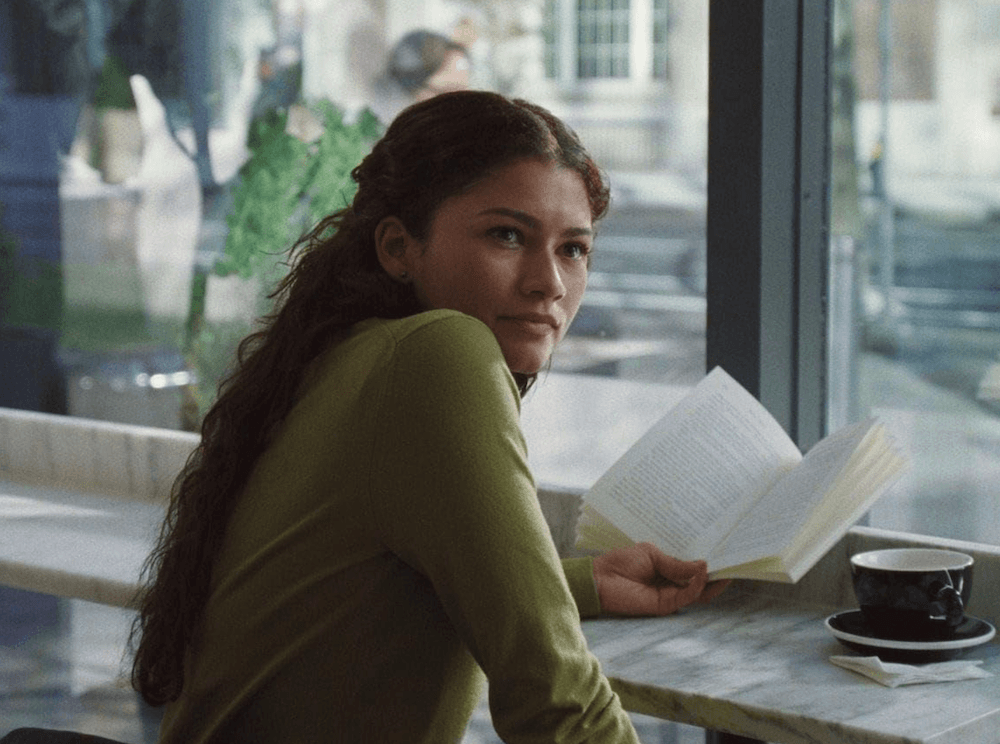 Emma (Zendaya) reading a fictional book called "The Damage" in a coffeeshop, in "The Drama." (A24)