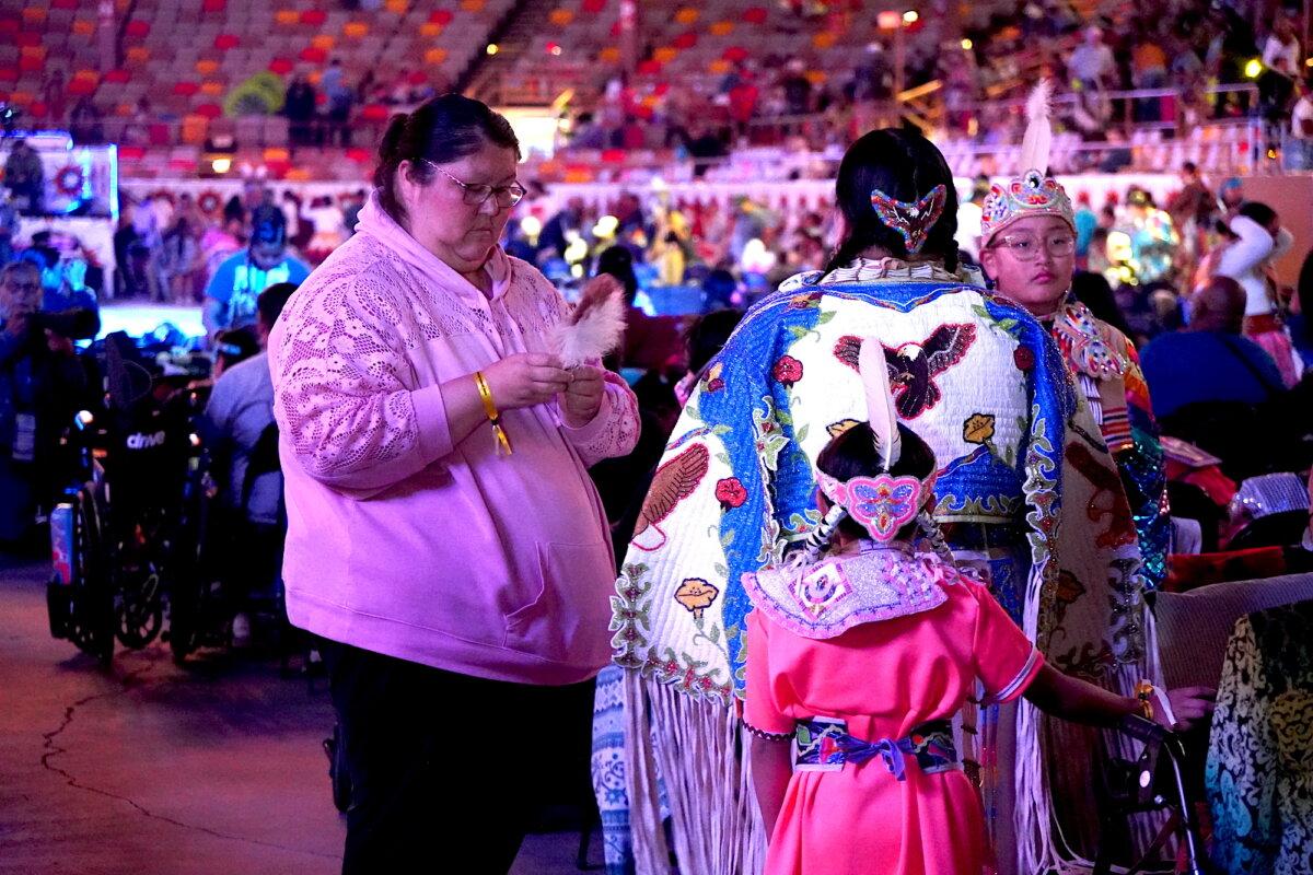 A woman helps participants adjust ceremonial dresses during the final Gathering of Nations powwow in Albuquerque, N.M., on April 24, 2026. (Allan Stein/The Epoch Times)