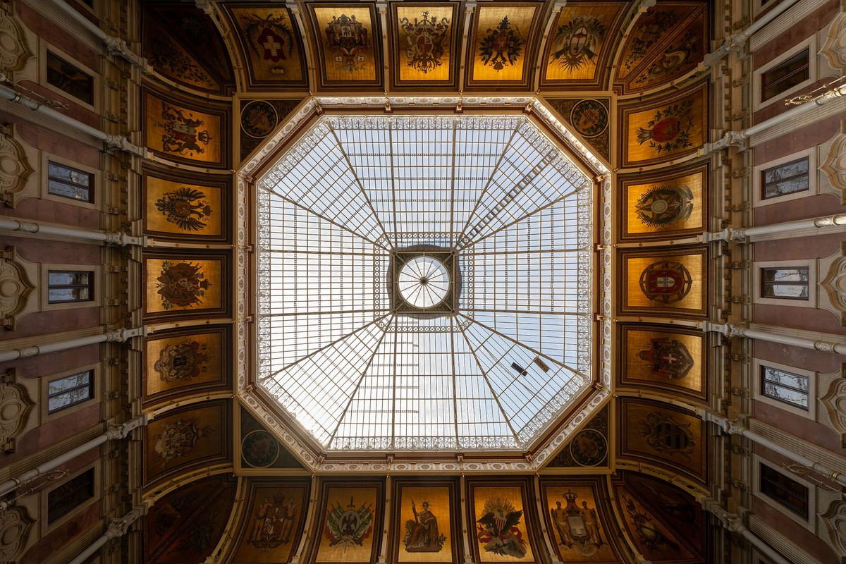 The multi-piece, octagonal-shaped glass ceiling allows natural light to flood the vast Courtyard of Nations. A complex iron framework of geometric shapes secures the pieces of glass. Yet, the standout artistic achievements are just below the dome: 20 painted coats of arms are set against a gilded backdrop and represent global countries with which Portugal has engaged in business. (Felix Lipov/Shutterstock)