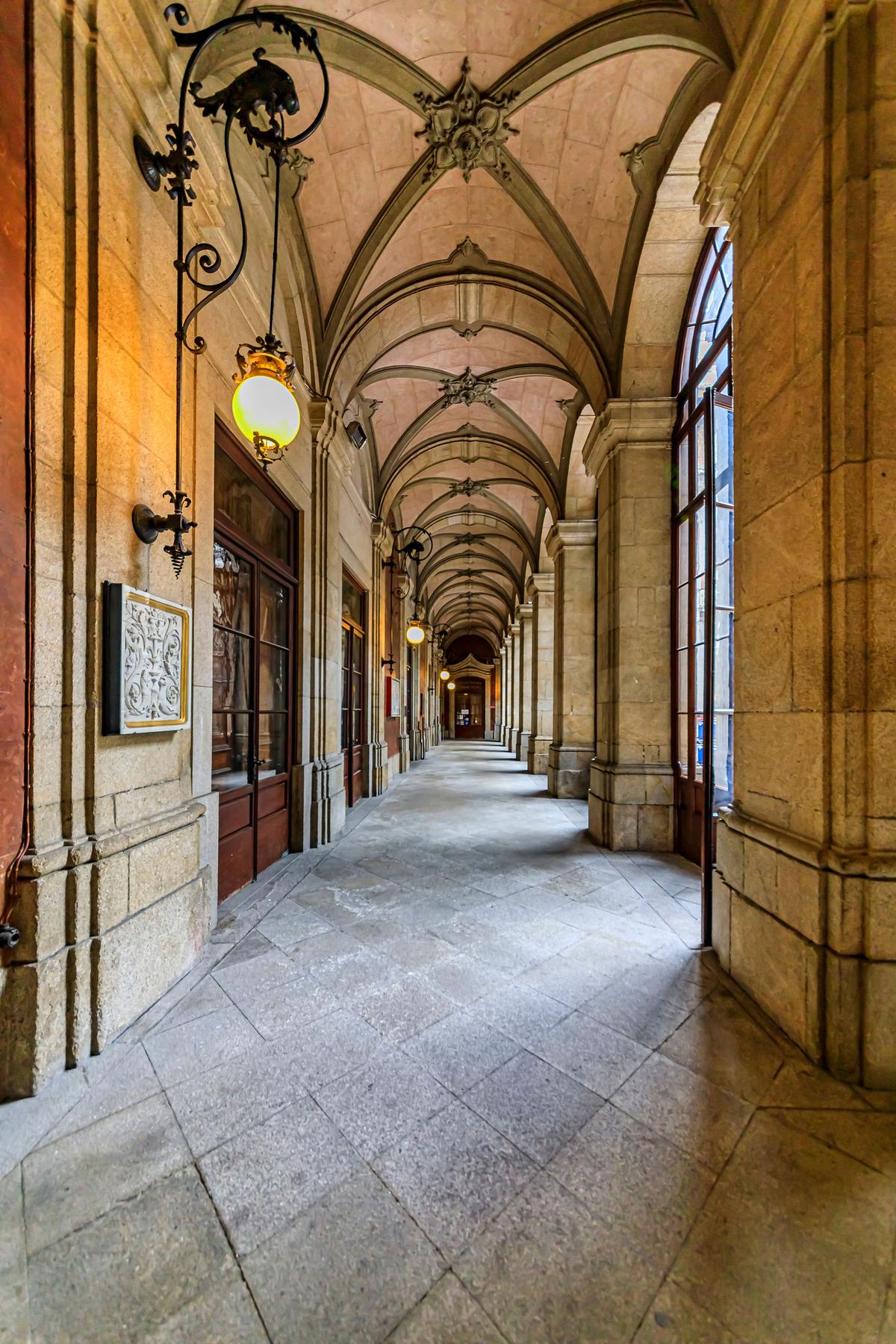 The Stock Exchange Palace’s most noteworthy hall features stone block columns flanking arched windows and a stone-block ceiling with rib vaulting. Each rib vaulting intersection is bedecked with carved keystones, also called bosses. Glass globe lighting fixtures hang from tall iron sconces. (SvetlanaSF/Shutterstock)