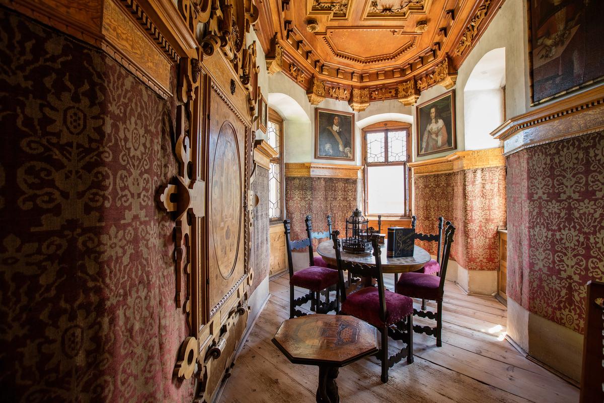 Executed in the High Renaissance style, the private Queen’s Chamber showcases exceptional craftsmanship. The chamber showcases an elaborately carved ceiling and original 1560 wall coverings adorned with a rich burgundy-and-gold damask pattern. Ancestral portraits and finely crafted wooden furnishings, including an octagonal occasional table, enrich the historic atmosphere. The dark wood chairs, upholstered in deep red velvet, echo the damask textiles, reflecting the queen’s status and refinement. (Courtesy of Schloss Tratzberg)