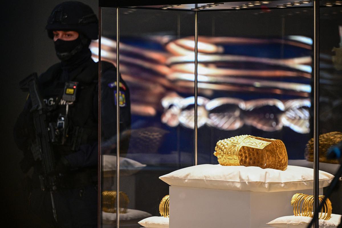 An armed police officer stands next to the ancient Cotofenesti helmet and two Dacian gold bracelets on display at the National Museum of History of Romania (MNIR) in Bucharest on April 21, 2026. (Daniel Mihailescu/Getty Images)