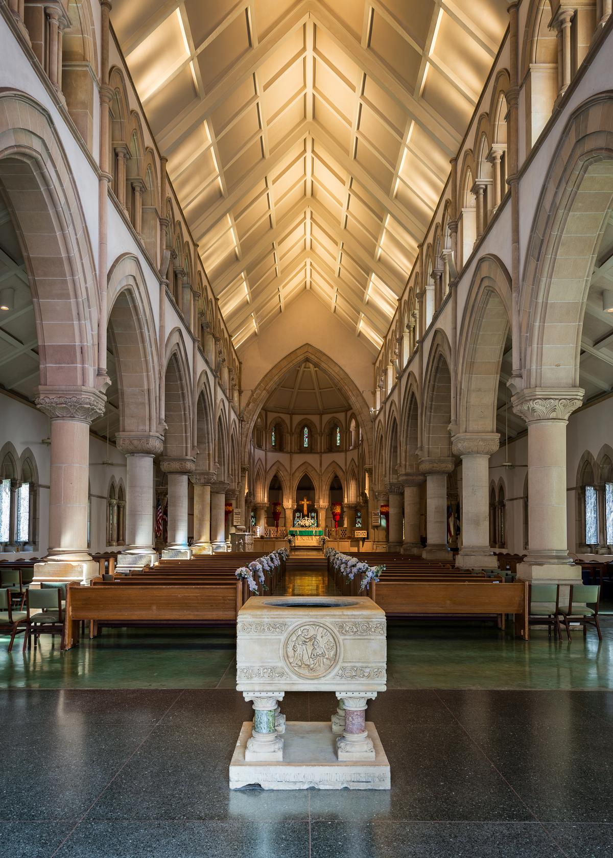 A more modern paneled and vaulted ceiling sits atop two stories of quintessentially Gothic pointed arches. The stone columns supporting the arches, in the ambulatory and clerestory areas of the cathedral’s sanctuary that lead to the chancel, have capitals decorated with stone carvings of both classical designs, such as acanthus leaves, and Hawaiian flowers and plants. The square baptismal font is carved from the same French quarried limestone as the altar: Caen stone. (Nagel Photography/Shutterstock)