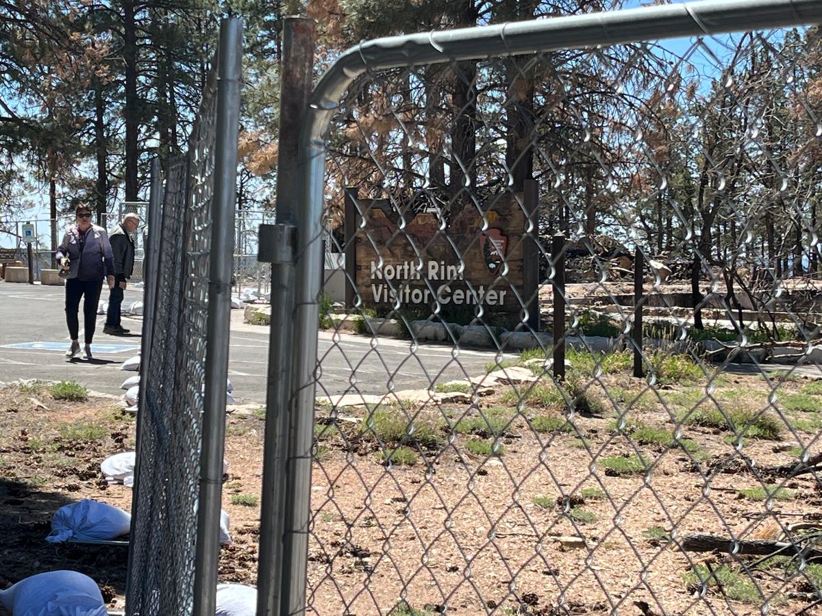Visitors stand outside the chain link fence shielding the remains of the Grand Canyon North Rim Visitor Center, Ariz., on May 19, 2026. (Allan Stein/The Epoch Times)