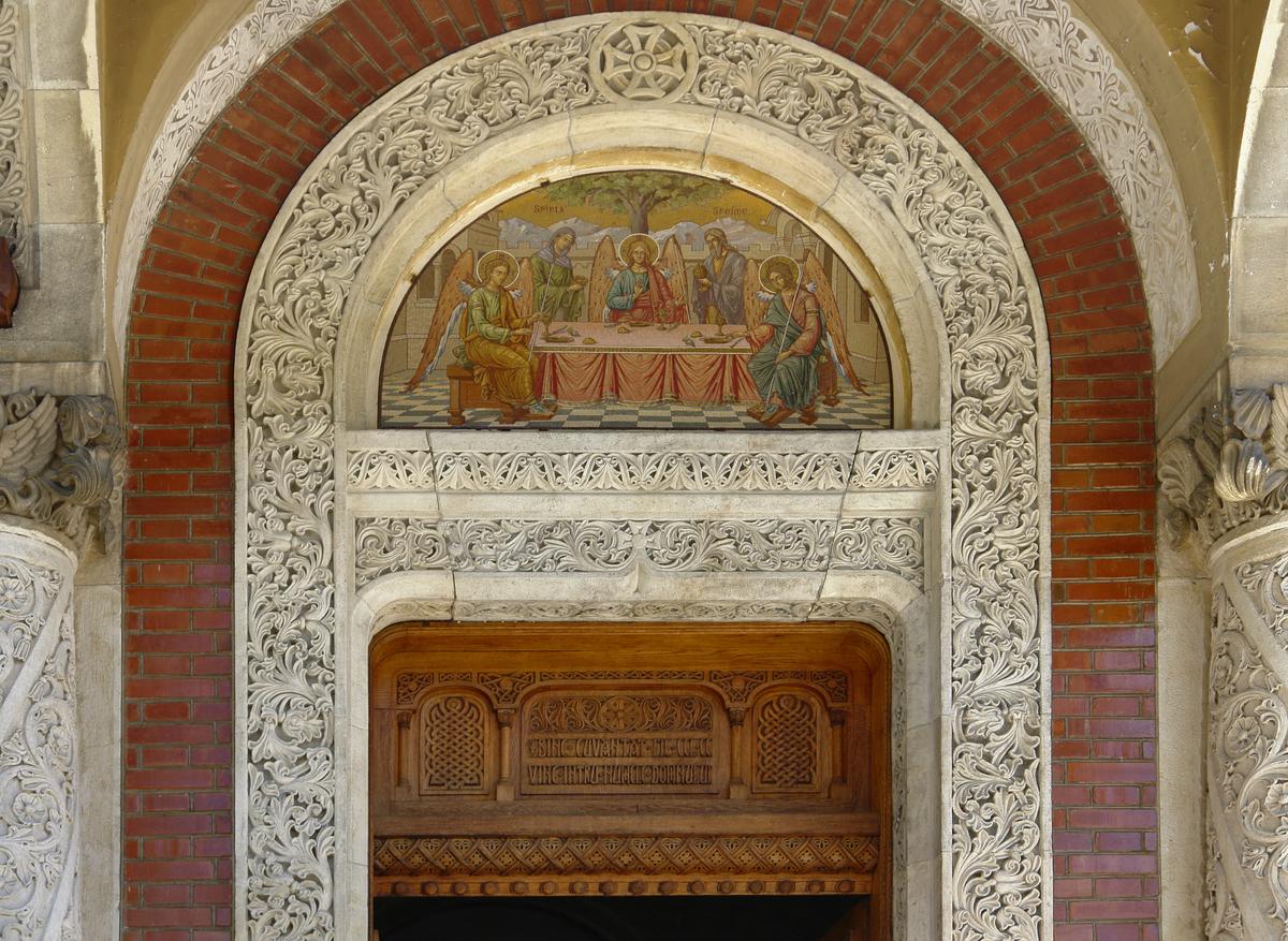 Above the entrance to the Great Church, a decorated semi-circular tympanum depicts the Holy Trinity, framed by densely carved foliate stonework and a medieval Christian cross. The tympanum is the ornamental space nestled between a doorway's horizontal lintel and the arch above it; here, it serves as a richly detailed focal point that welcomes visitors into the sacred interior. (Prill/Shutterstock)