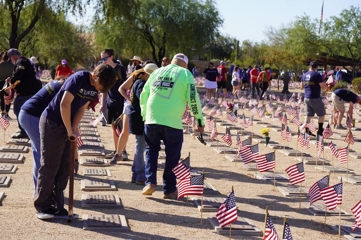 Volunteers from across Arizona place hundreds of flags beside veterans' grave markers at the National Memorial Cemetery of Arizona in Phoenix on May 23, 2026. (Allan Stein/The Epoch Times)