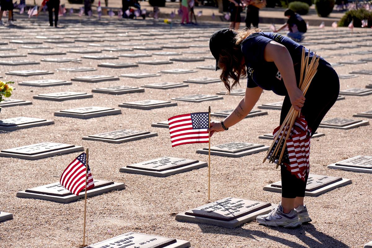 A volunteer places a flag beside a grave marker at the National Memorial Cemetery of Arizona in Phoenix on May 23, 2026. (Allan Stein/The Epoch Times)