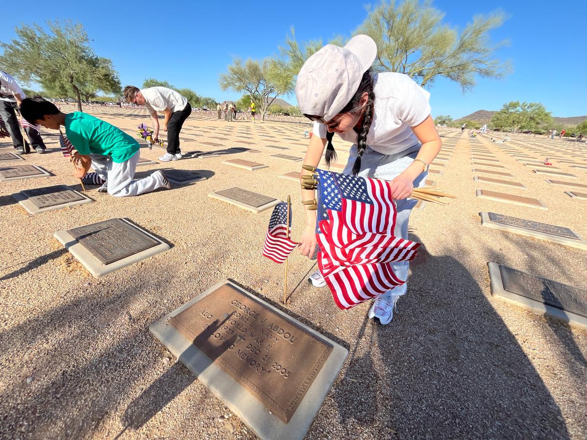 A young volunteer places a flag beside a veteran grave marker in Phoenix on May 23, 2026. (Allan Stein/The Epoch Times)