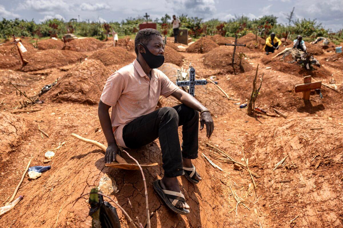Bora Moise sits beside the grave during the funeral of his late nephew Baraka Ngaju during the Ebola outbreak, at a cemetery in Mongbwalu, Ituri province, Congo, on May 20, 2026. (Michel Lunanga/Getty Images)