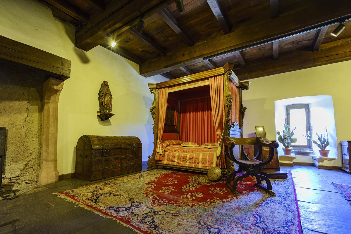 Thick wooden beams conveying Renaissance aesthetics are prominent in this Vianden Castle bedroom. Also indicative of Renaissance style is the bedroom’s red-and-gold color scheme in the bed canopy's fabric and the Oriental carpet. The rustic fireplace features a wood-beam mantel and is flanked by carved stone columns. (Kit Leong/Shutterstock)