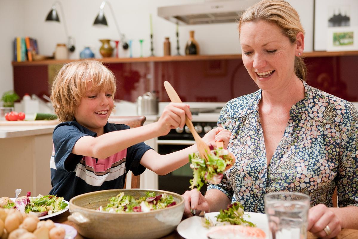 A son helps serve salad to his mother. Respect, helpfulness, and consideration for others are values often taught through family traditions. (Connect Images/Getty Images)