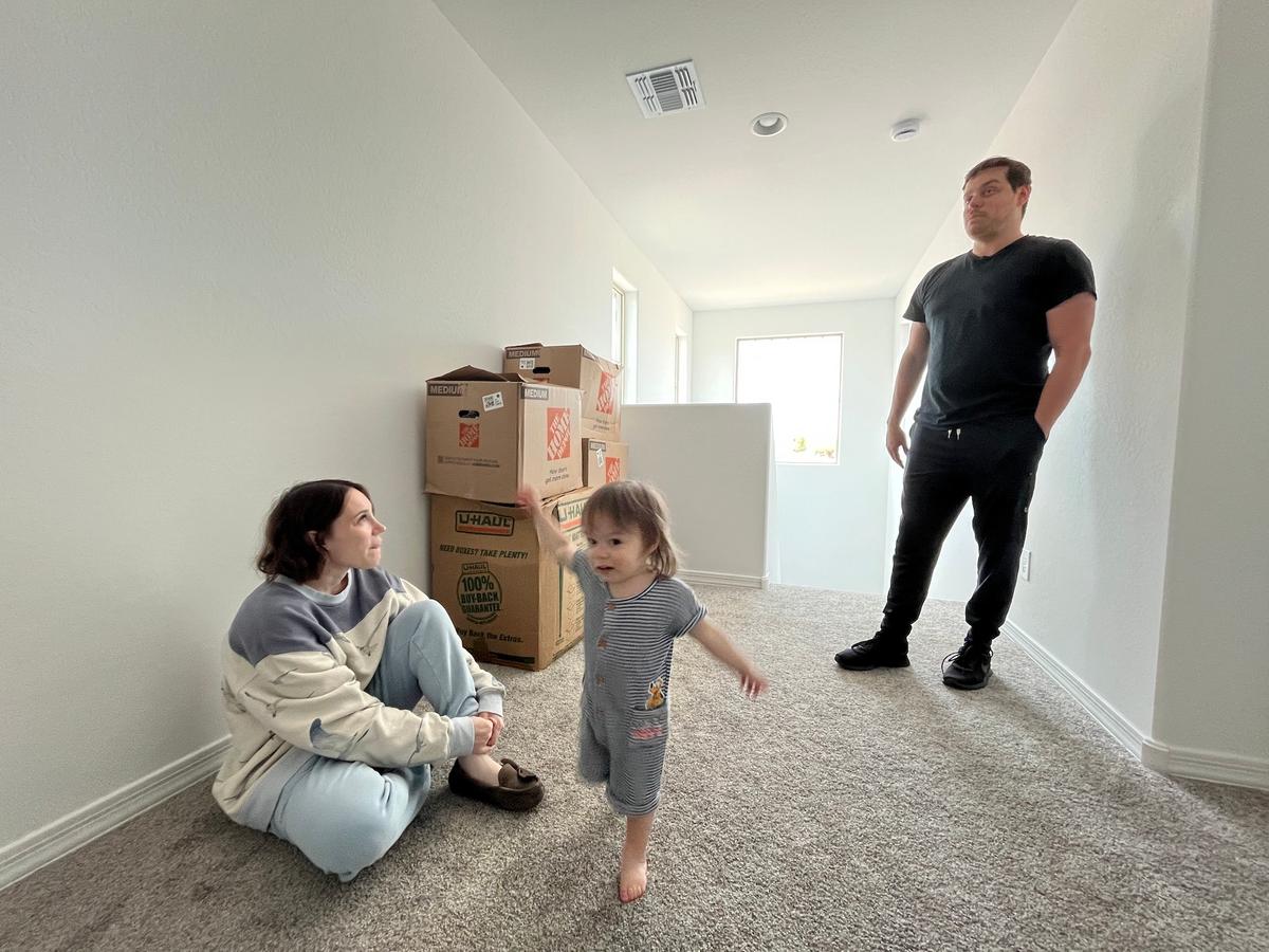 Annabelle Mattaliano (L), her husband Padge Mattaliano, and their 18-month-old son Fox stand in the hallway on the second floor of their new mortgage-free home in Avondale, Ariz., on June 6, 2026. (Allan Stein/The Epoch Times)