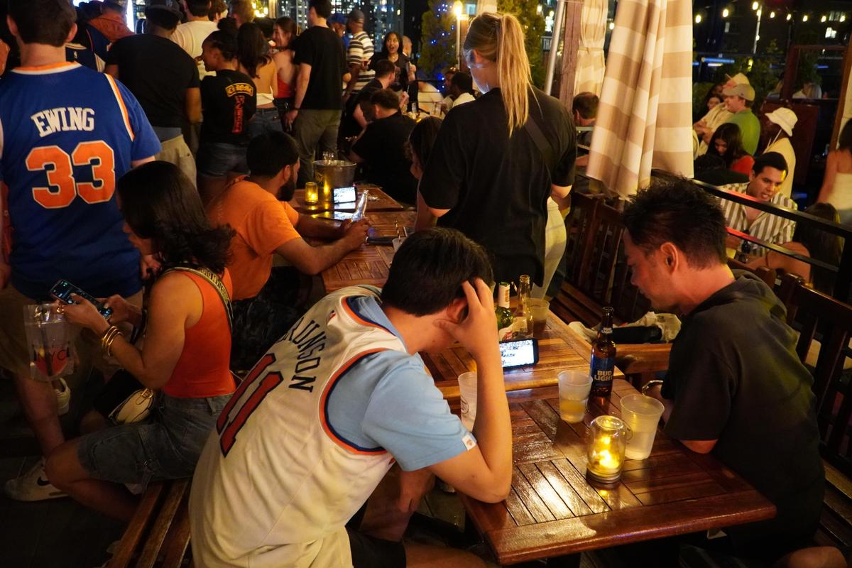 Fans watch the NBA Finals game of the Knicks vs. the Spurs in Game 5 at a rooftop bar in Manhattan, N.Y., on a cell phone June 13, 2026 (Nicholas Zifcak/The Epoch Times)