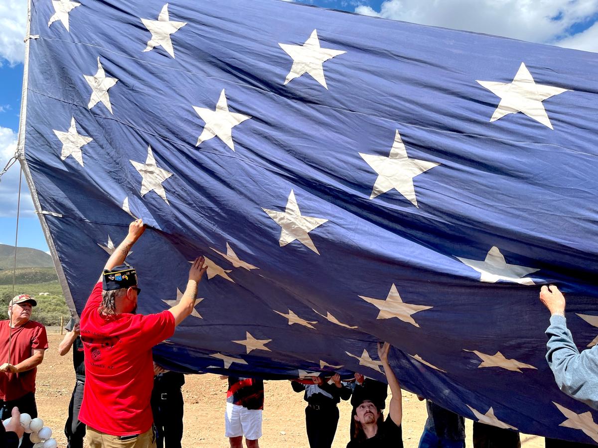A volunteer helps prevent Old Glory from touching the ground as it is hoisted during a Flag Day ceremony in Mayer, Ariz., on June 14, 2026. (Allan Stein/The Epoch Times)