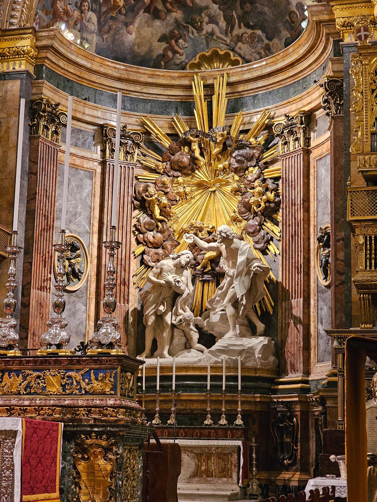 Installed in 1689, the high altar combines marble, gilded bronze inlay, semi-precious stones, and lapis lazuli to create a richly luminous focal point within the sanctuary. Beyond it, in the apse, stands Giuseppe Mazzuoli’s monumental Carrara marble sculptural group depicting the Baptism of Christ, one of the cathedral’s most impressive artistic achievements. (Sujin Krishnan/Shutterstock)