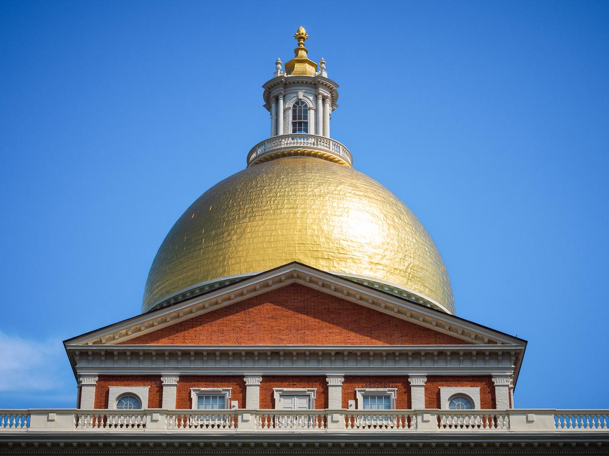 The Massachusetts State House is crowned by its celebrated gilded dome, a defining feature of its Federal-style design. At the summit, a circular lantern brings in natural light and completes the dome’s vertical axis, while a pine cone finial serves as a symbolic capstone, finishing the composition with a distinctive touch. Beneath the dome is a low-pitched triangular pediment, functioning as a transition piece and common in Federal-style architecture. (Victor F Rodriguez Jr/Shutterstock)
