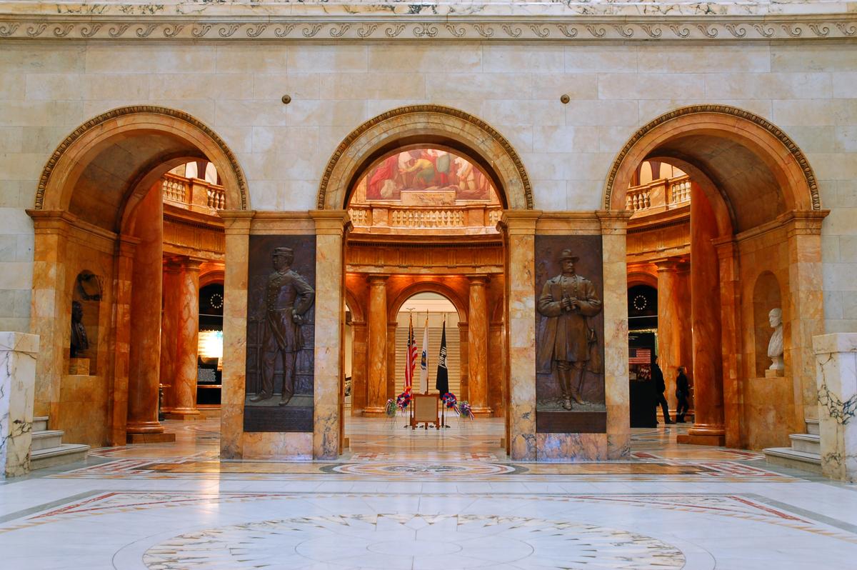 Marble detailing frames the entrance to the rotunda, while doorways and arches feature wood framing reinforced with metal hardware, reflecting 19th-century upgrades. Positioned beneath the building's gold dome, the rotunda marks the exact seam where the original State House meets its rear addition, making it the architectural hinge of the complex: to cross through is to walk from old into new. (James Kirkikis/Shutterstock)