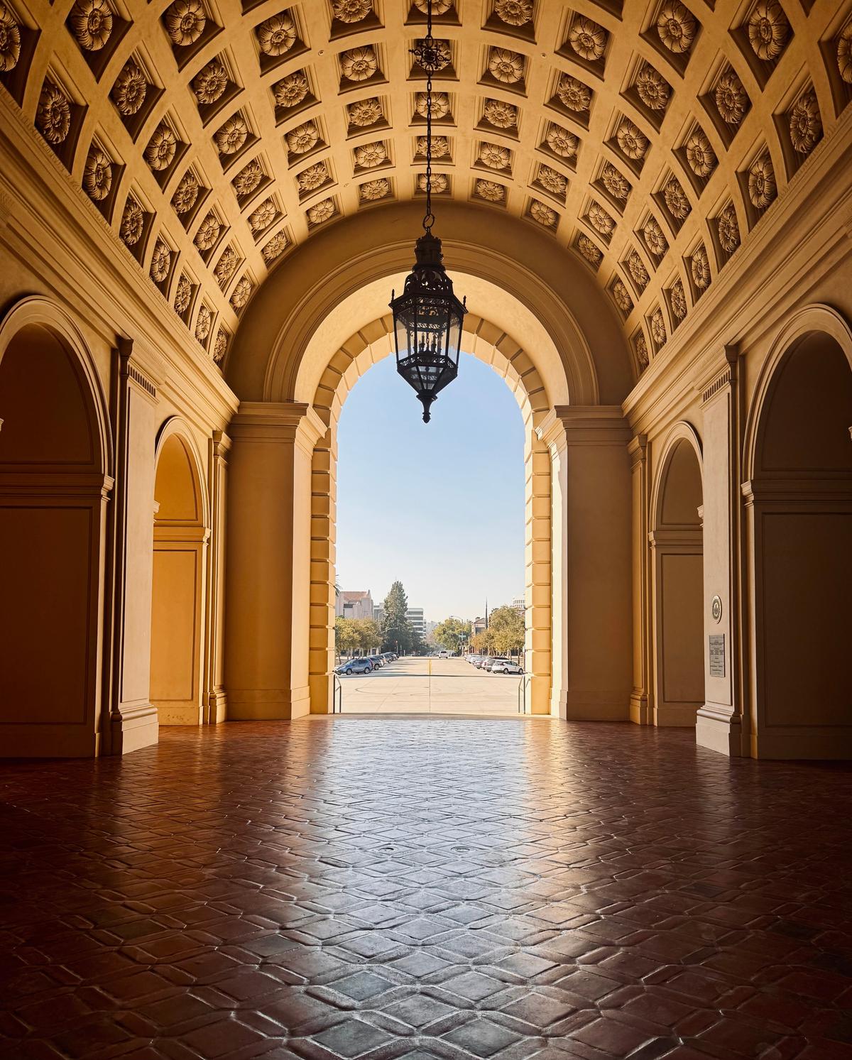The east side of Pasadena City Hall’s courtyard is a one-story cloistered arcade, or a covered walkway that features a succession of contiguous arches that leads outside. The arcade has a red tile floor, square columns with Doric capitals at the arched opening, and pilasters defining its many arches. The barrel-vaulted ceiling is apportioned with caissons, meaning square inset boxes, which serve as frames for rosettes. (Form and Flora/Shutterstock)