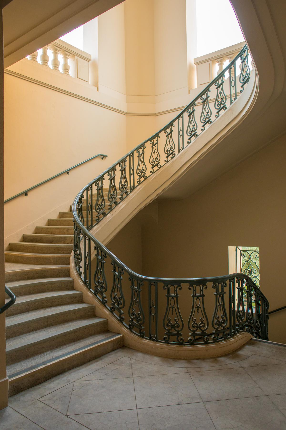 Balustrades surround the different levels of the main staircase. The curvaceous floating staircase has marble treads and a wrought iron banister, which features a classic design that resembles an ancient lyre. (Justin Ta/Shutterstock)