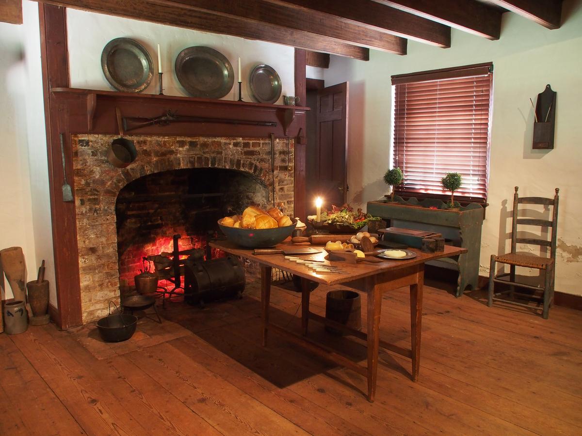 The kitchen features poplar wood beams, heart pine flooring, and a brick fireplace. Displayed on the wood mantel are pewter trays. In the colonial era, pewter was often preferred as a more durable, higher-end material than wood for serving and dishware, yet it was less expensive to make and purchase than silver. Against the wall is a ladder-back chair with a woven rush seat. (Courtesy of Historic Odessa Foundation)