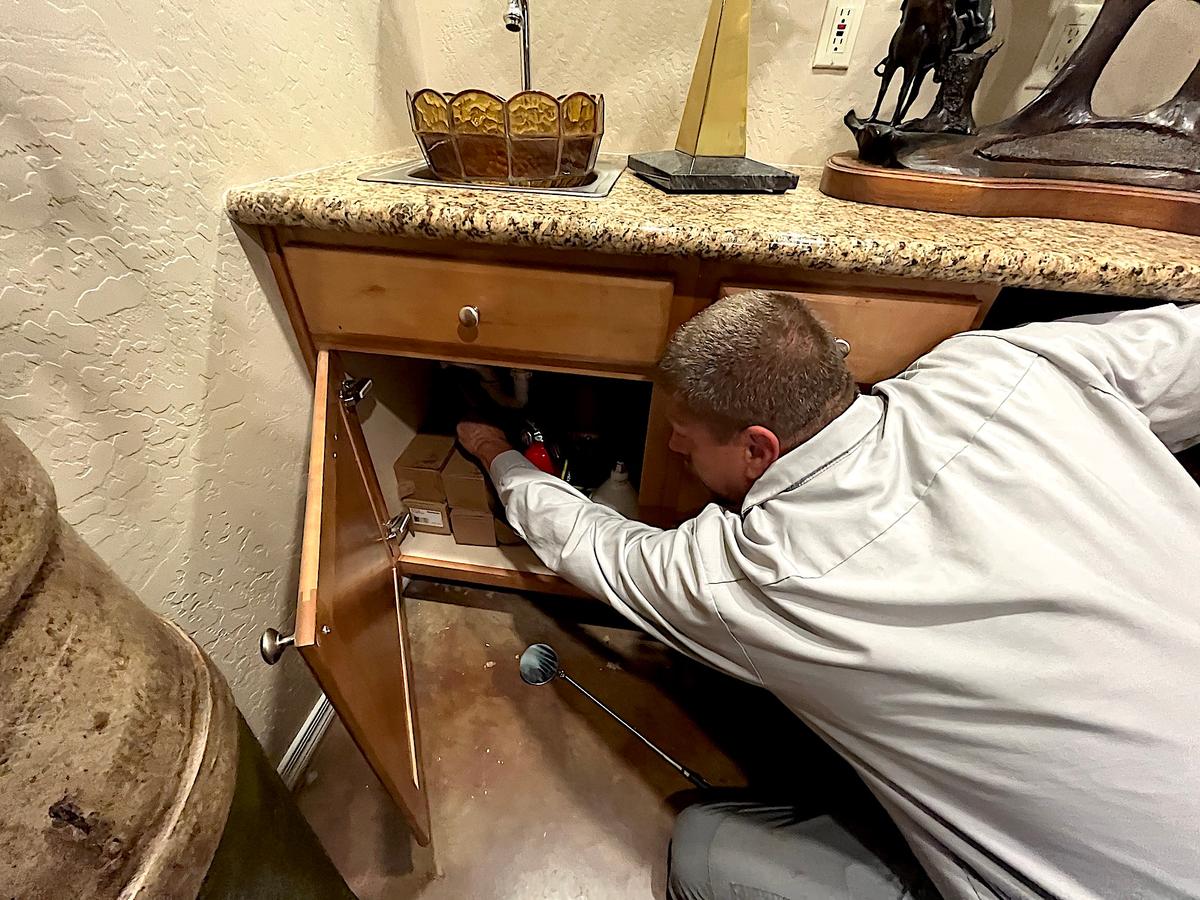 Senior scorpion specialist Mike Golleher checks for scorpions under the kitchen sink in Tempe, Ariz., on June 24, 2026. (Allan Stein/The Epoch Times)