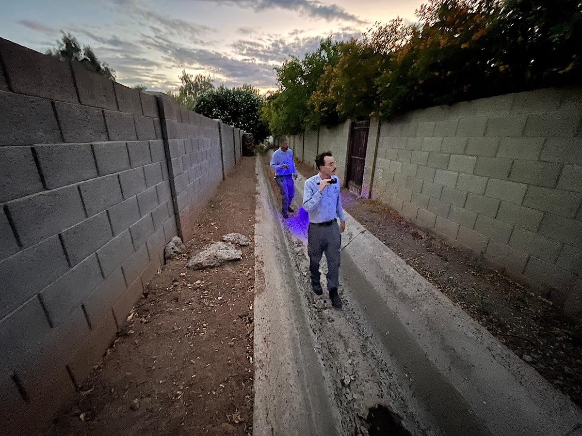 Jeremiah Sourp (R) and Mike Golleher walk looking for scorpions along the concrete drainage canal behind a residential neighborhood in Tempe, Ariz., on June 24, 2026. (Allan Stein/The Epoch Times)