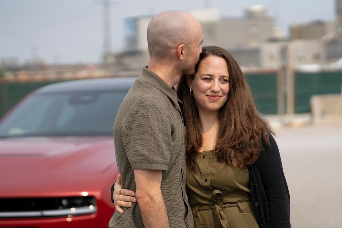 Gordie Howe's grandson, also named Gordie, and his wife Margaret (R) pose in front of a Dodge Charger, before driving it across the Gordie Howe International Bridge on July 27, 2026. (Windsor-Detroit Bridge Authority)