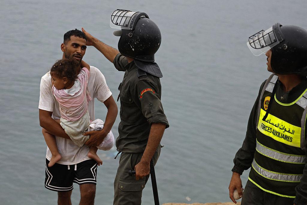 A member of Moroccan security forces gestures to a man carrying a child close to the site of clashes near Fnideq, on the Morocco–Spain border, on July 31, 2026. (Abdel Majid Bziouat/AFP via Getty Images)