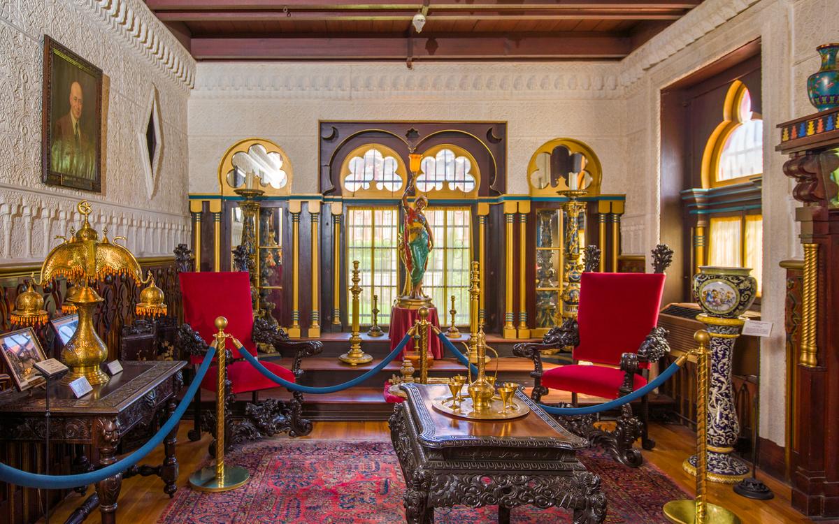 Named by Smith as the Hall of Justice after a room in the Alhambra, this space was once used as Villa Zorayda’s dining and living room. Since the mansion became a museum in 1933, the space presents various art and furnishings, including an Egyptian maiden lamp statue, which includes a signed Tiffany shade. Five-foot candleholders are positioned in front of floor-to-ceiling mirrors set within arches. These match the pair of windows, which are framed by wood carved with sun and crescent moon designs. Slender gilded columns are built into the walls, which are plastered in arabesque decorations of interlacing foliage and Moorish-style scrollwork and motifs. (Villa Zorayda Museum)