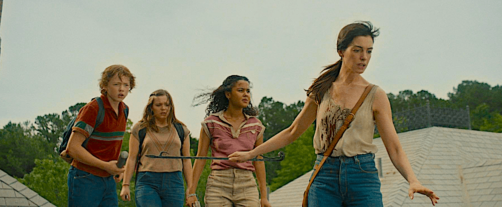 (L–R) Brian (Christian Convery), Audrey (Maisy Stella), Jeanette (Jordan Alexa Davis) and Denise (Anne Hathaway) try to escape marauding dinosaurs by climbing on the roof, in “The End of Oak Street.” (Warner Bros. Pictures)