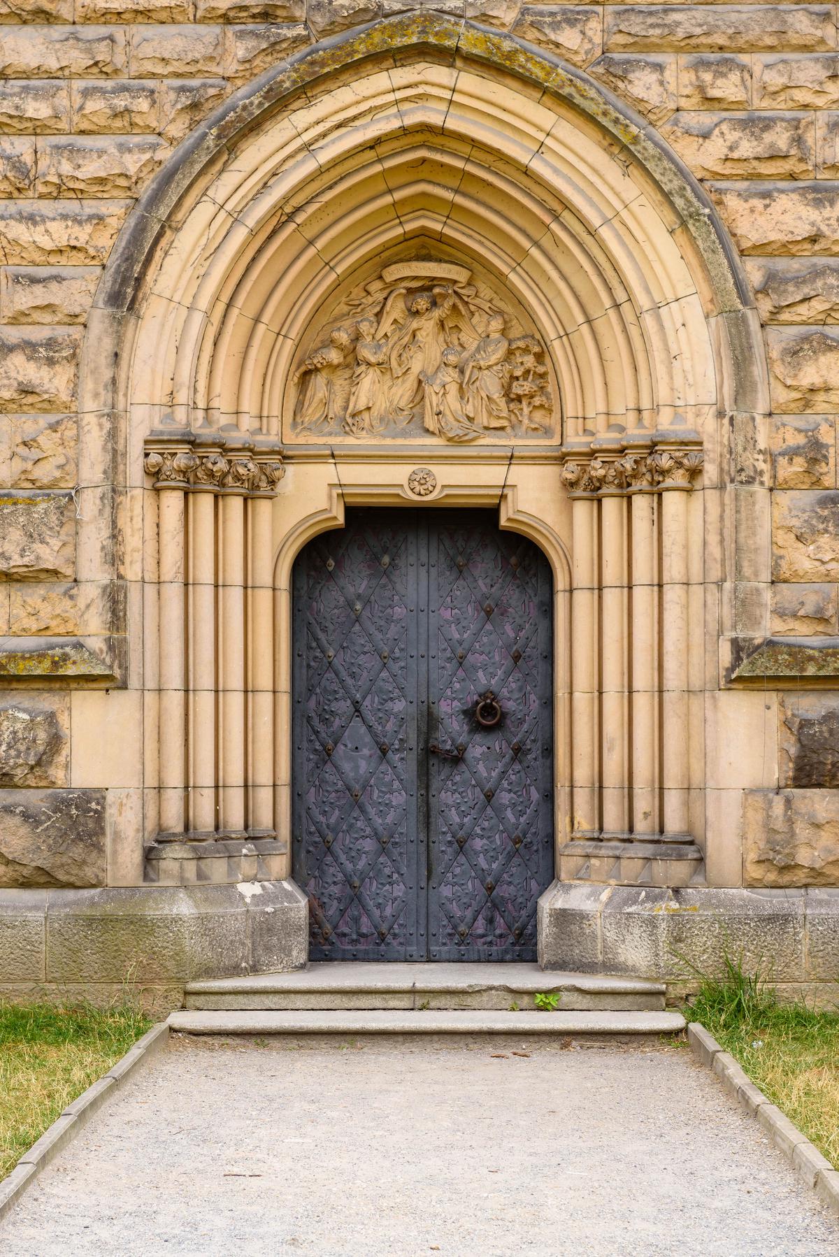 What was once a Lutheran chapel is now a venue for various events. However, details such as the multi-layered, inset Gothic-arched door featuring a carved stone bas-relief of a biblical scene remind visitors that this was once a house of worship. The pointed Gothic arches are supported by four, inset slender columns with Corinthian capitals. The arches symmetrically flank the hand-hammered steel, double door, which is affixed with a medieval-style round door knocker. A carved rosette accentuates the center point of the door frame. (vivooo/Shutterstock)