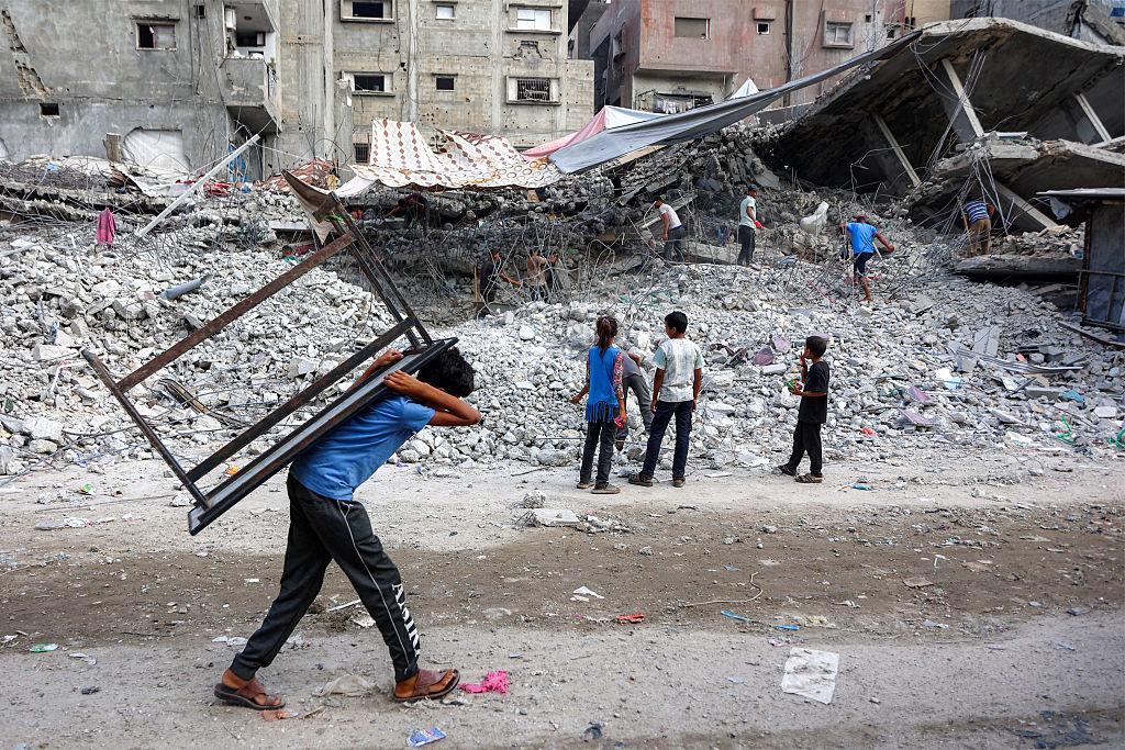 A boy walks carrying a table on his back past salvage workers scrapping the rubble of a building that was destroyed during Israel's war against Hamas in Gaza, to use the recycled remains in the future, in Gaza City on Aug. 16, 2026. (Omar Al-Qattaa/AFP via Getty Images)