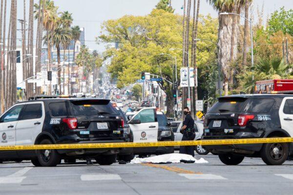 LAPD police officers stand at the corner of Fairfax Avenue and Sunset Boulevard where a body covered in a white sheet lies on the pavement in Los Angeles on April 24, 2021. (VALERIE MACON/AFP via Getty Images)