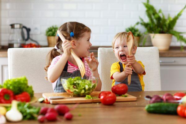 Happy children prepares and eats vegetable salad. (Shutterstock)