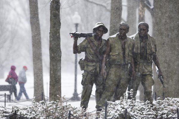 Visitors walk past the "The Three Soldiers" statue that is part of the Vietnam Veterans Memorial during a snowstorm in Washington, Tuesday, March 25, 2014. (AP Photo/ Evan Vucci)