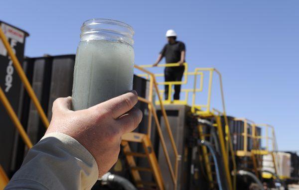A jar holding waste water from hydraulic fracturing is held up to the light at a recycling site in Midland, Texas, Sept. 24, 2013. The drilling method known as fracking uses huge amounts of high-pressure, chemical-laced water to free oil and natural gas trapped deep in underground rocks. With fresh water not as plentiful, companies have been looking for ways to recycle their waste. (AP Photo/Pat Sullivan)