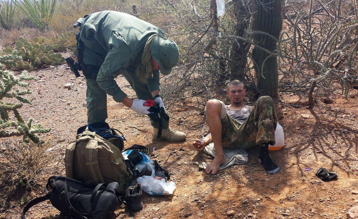 An unidentified US Border Patrol agent (L) helps an immigrant, including setting up intravenous fluid replacement for dehydration, near Sells, Ariz., on June 25, 2014. (Astrid Galvan/AP Photo)